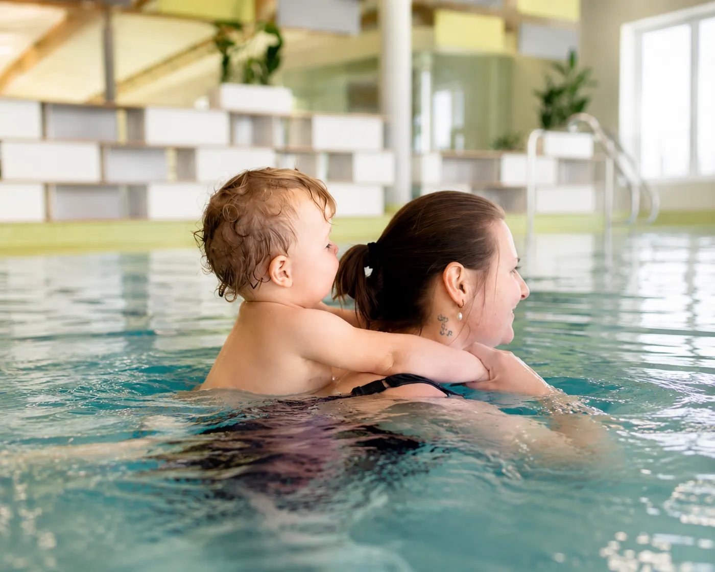 Kleinkind hält sich im Schwimmbecken am Rücken seiner Mutter fest